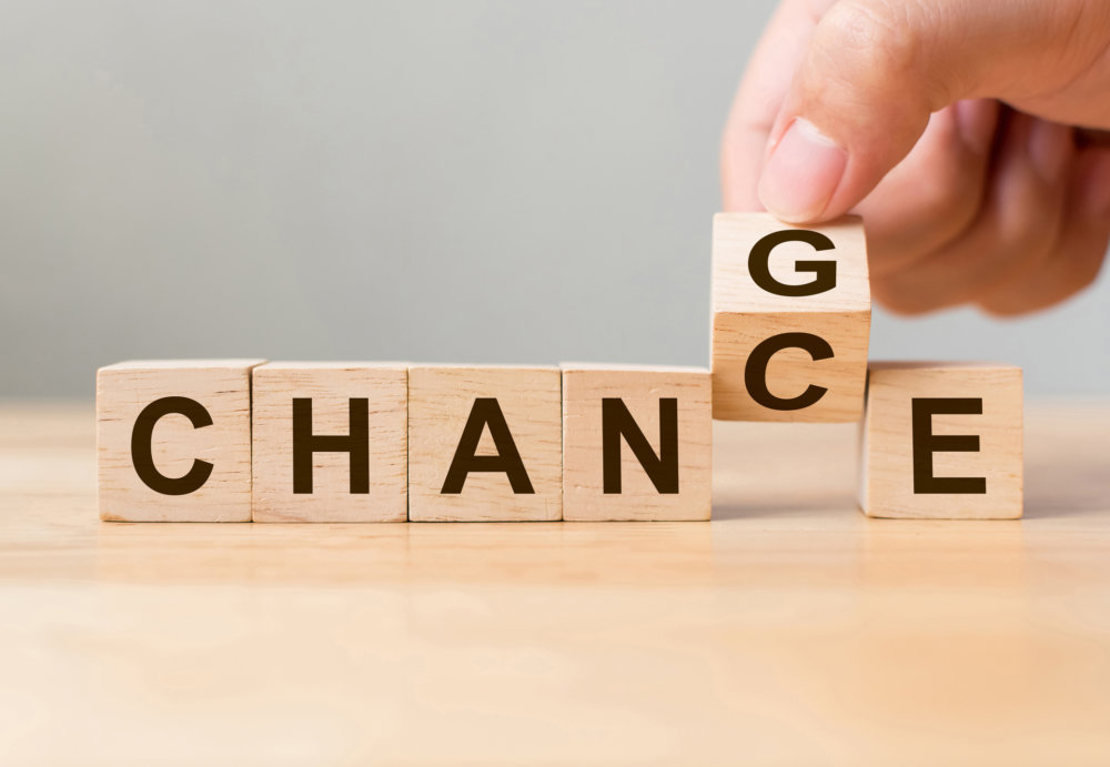 Eine Hand dreht einen Holzklotz mit dem Buchstaben G, um das Wort CHANGE in CHANCE auf einer hellen Holzoberfläche zu verwandeln, was die Möglichkeit für Wachstum und Transformation im Network Marketing symbolisiert.