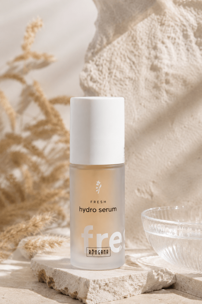 Ein Fläschchen Fresh Hydro Serum von RINGANA Frischekosmetik steht auf einer strukturierten Steinfläche mit einem Glasschälchen daneben vor einem hellen, natürlichen Hintergrund mit zarten Trockenpflanzen.